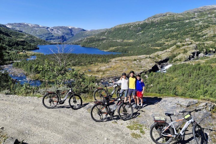 A group of people with bicycles on a rocky terrain overlooking a lake and mountains. 1
