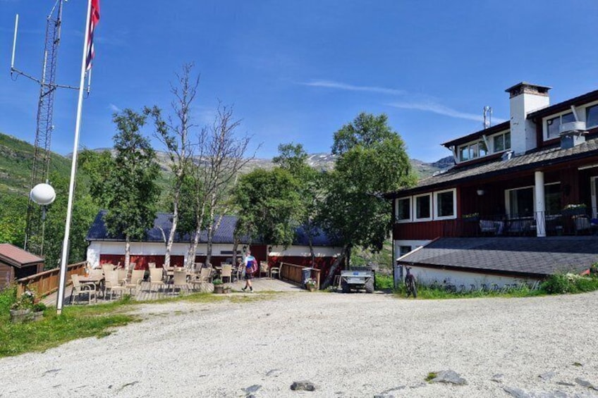 A rural setting with a gravel path, wooden buildings, and a flagpole. 4