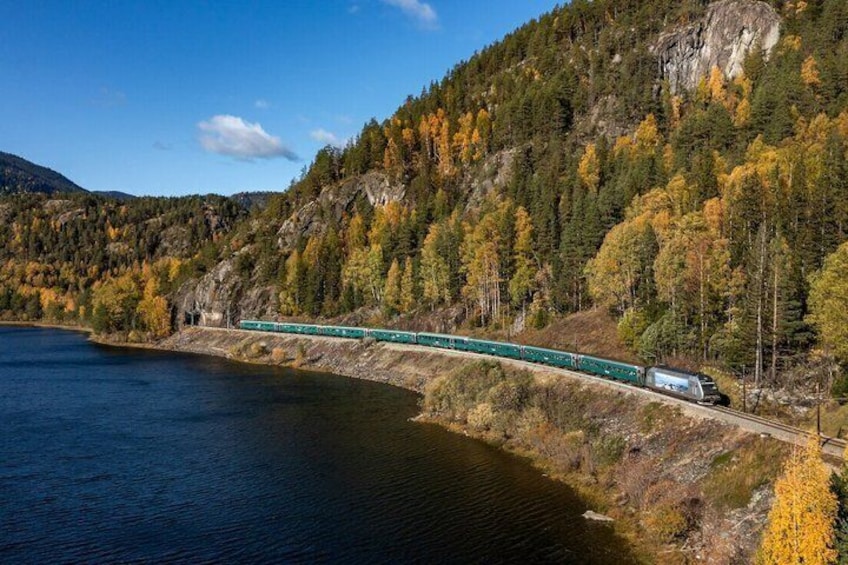 A train on a bridge over a lake, surrounded by autumn-colored trees and a mountainous landscape. 5
