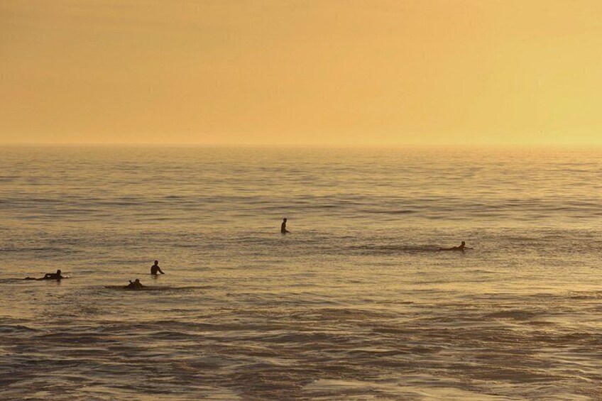 Ein Sonnenuntergang über dem Meer mit Menschen beim Schwimmen und Surfen. 4
