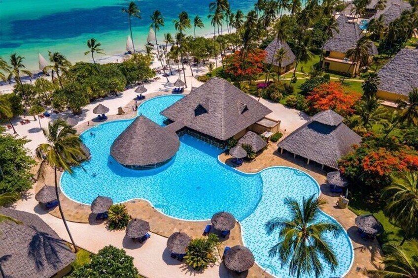 A resort with a large swimming pool surrounded by palm trees and thatched-roof huts. 4