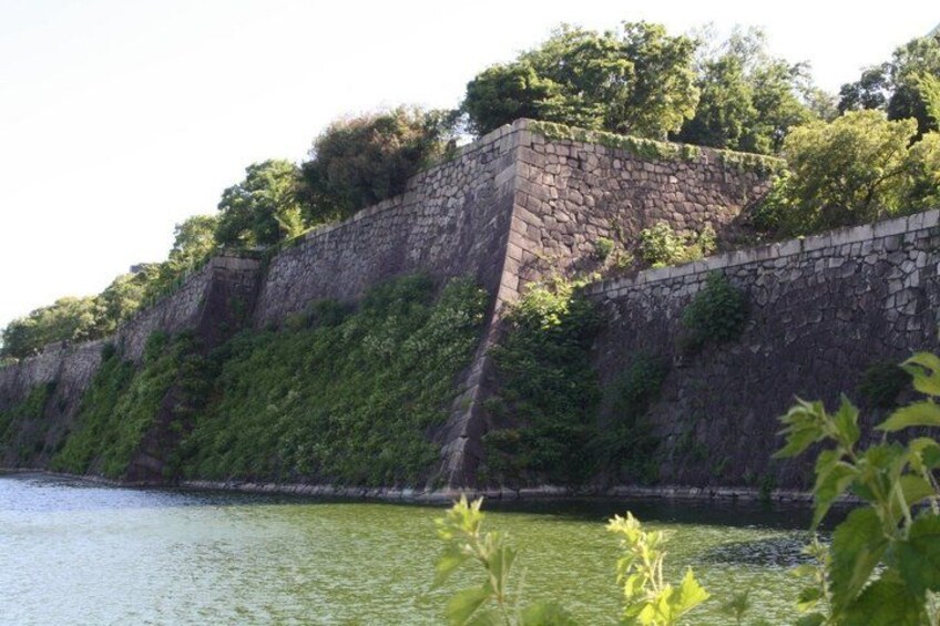 Eine steinerne Mauer mit Grünpflanzen, ein Gewässer und ein klarer Himmel. 4