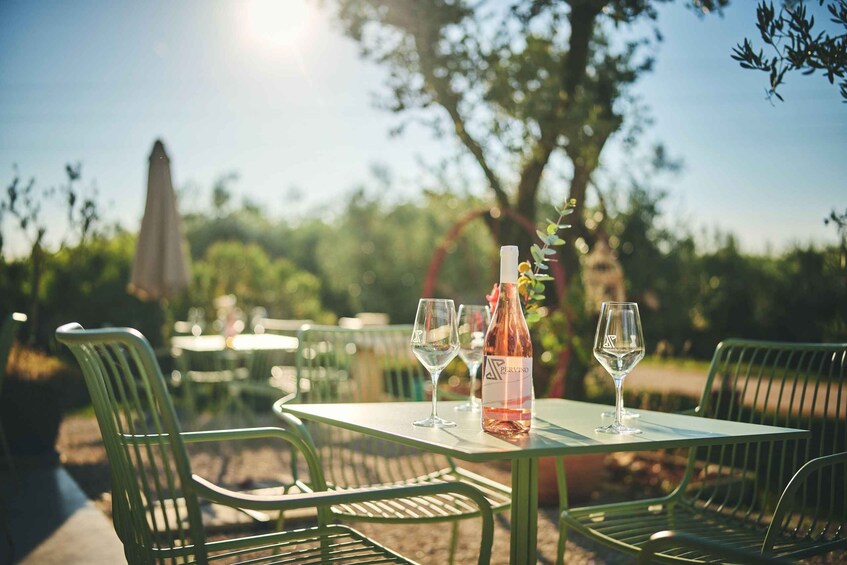 An outdoor dining area with green metal chairs and tables, a bottle of wine, and a glass on one table. 1