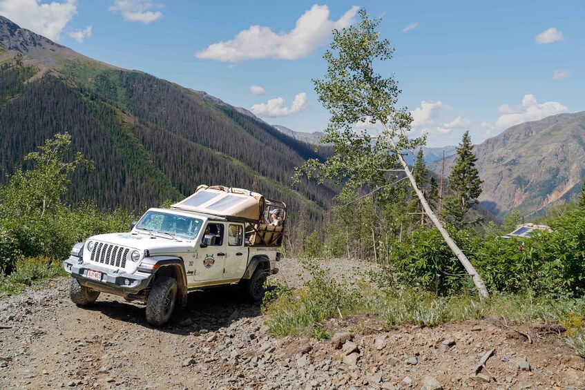 A white off-road vehicle with a roof rack parked on a rocky trail in a mountainous area. 5