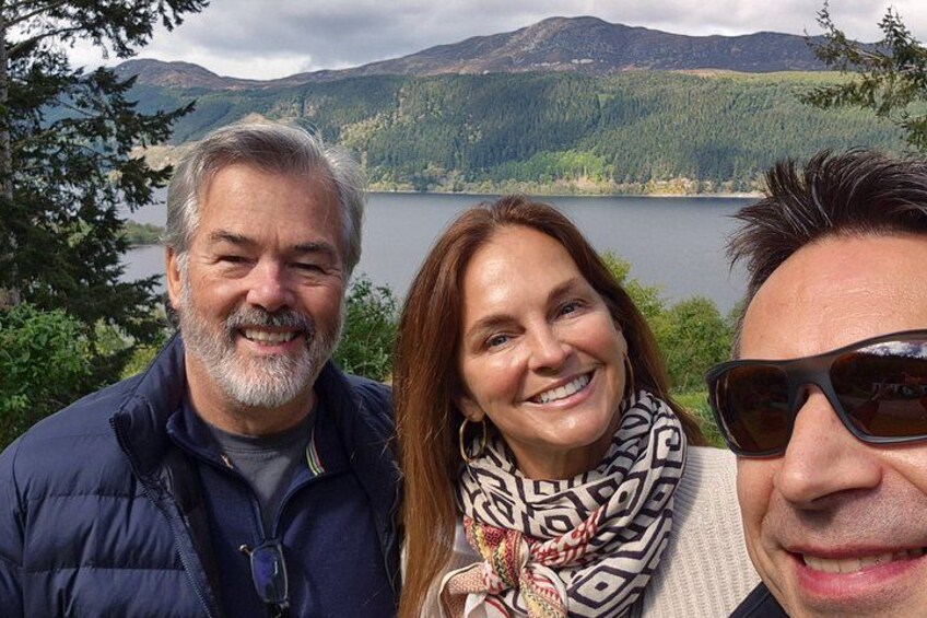 Tre persone in piedi di fronte a un lago con montagne sullo sfondo. 3