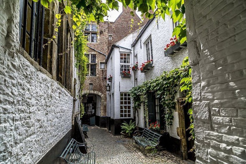 A narrow cobblestone alley with white buildings, a bench, and red flowers in window boxes. 4