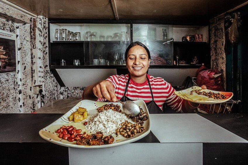 A person serving food from a large plate with various items including rice, beans, and vegetables. 1