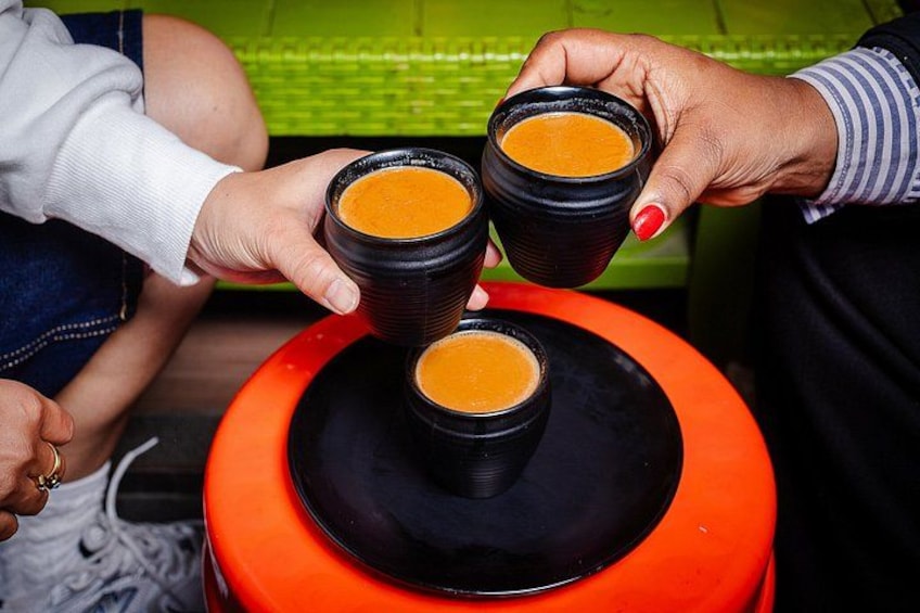 Three people holding black cups with orange liquid, likely coffee or tea, on a red stool. 3