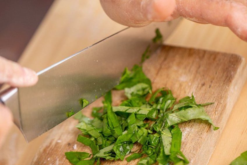A person chopping green herbs on a wooden cutting board. 4
