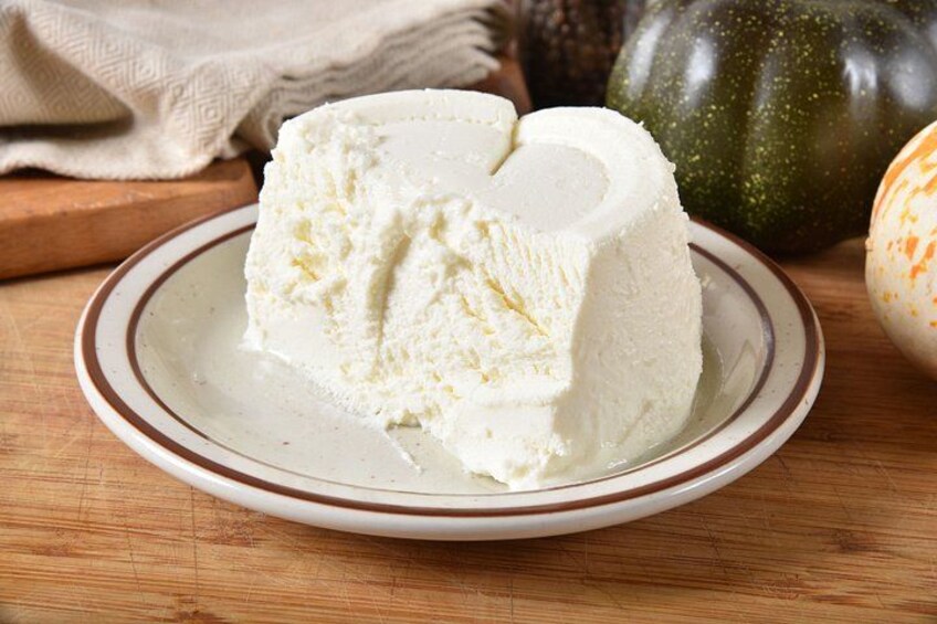 A block of white cheese on a plate with a brown rim, placed on a wooden surface. 4