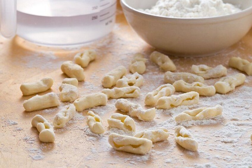 Uncooked pasta shapes on a floured surface with a measuring cup and a bowl of flour in the background. 2