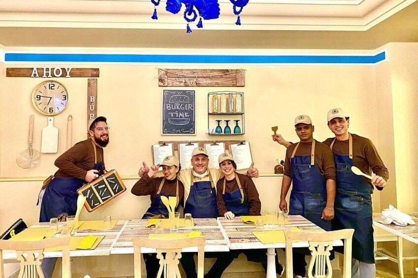Un grupo de personas con mandiles sentadas a una mesa con un menú, un reloj y un cartel que dice 'BURGER TIME'. 5