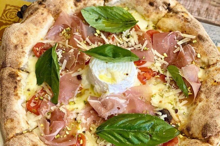 Una pizza con ingredientes como queso, tomates, albahaca y jamón prosciutto. 2