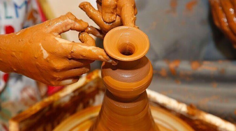 Hands shaping a clay pot on a pottery wheel. 4