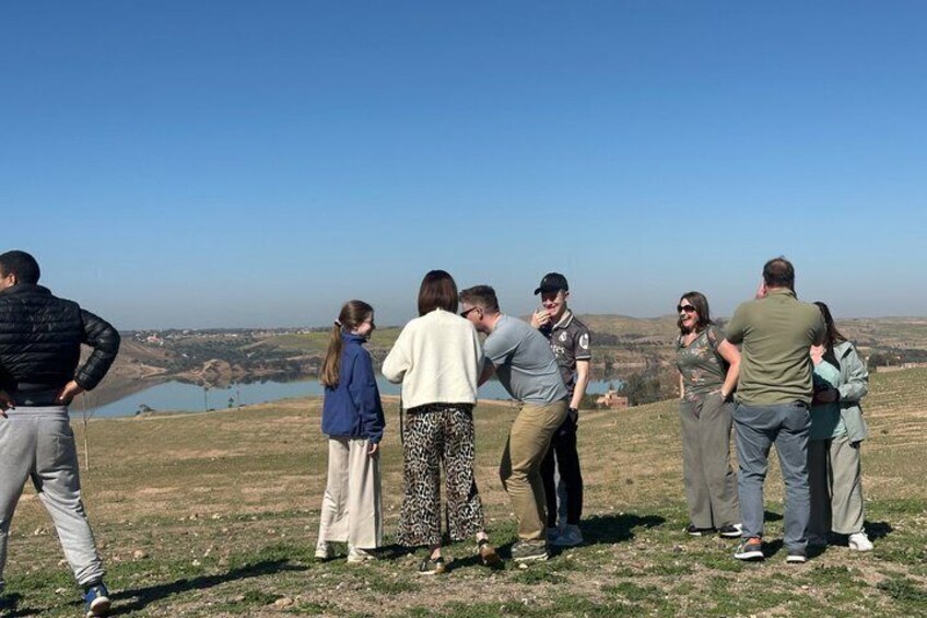 A group of people standing on a grassy hill overlooking a body of water and distant landscape. 2