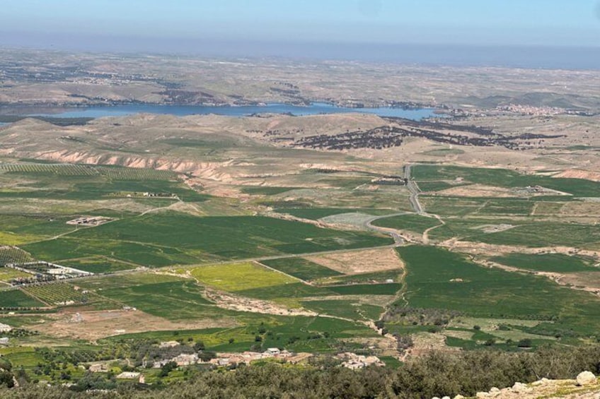 A vast agricultural landscape with terraced fields, a winding road, and a distant body of water. 3