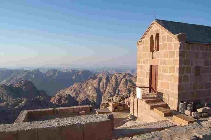 A stone building with a door, surrounded by a stone wall, overlooking a mountainous landscape. 2