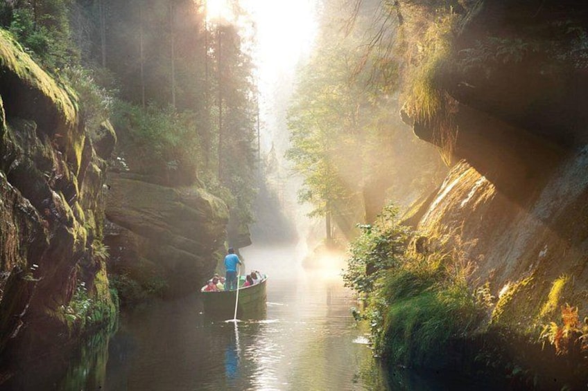 A narrow river with a boat carrying people, surrounded by rocky cliffs and dense greenery. 4