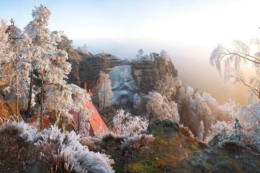 A frost-covered landscape with a red-roofed building, trees, and a rock formation. 3