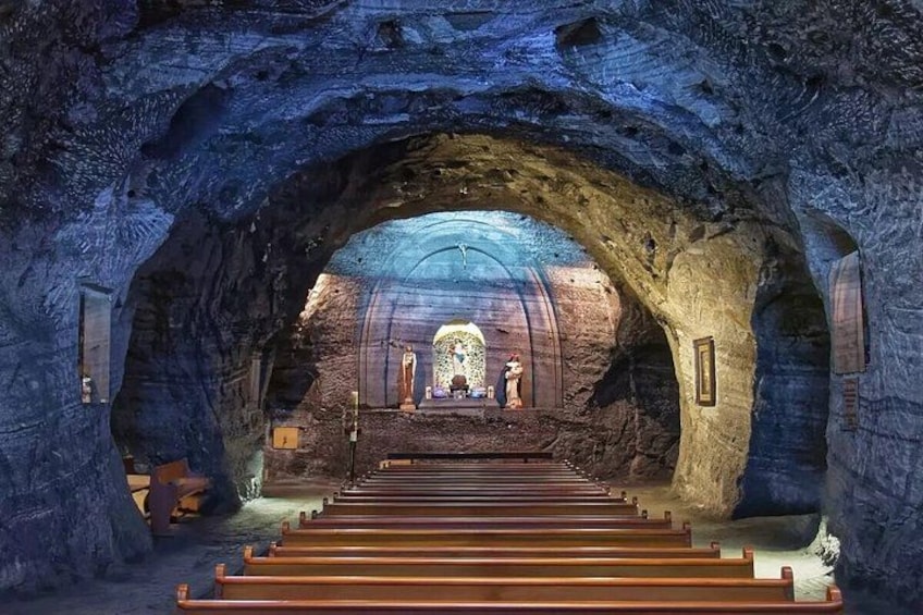 An underground church with a central altar, stone walls, and wooden pews. 1