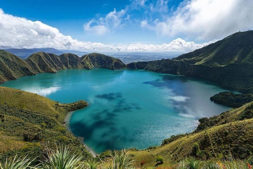 A turquoise lake surrounded by green hills under a clear sky. 3