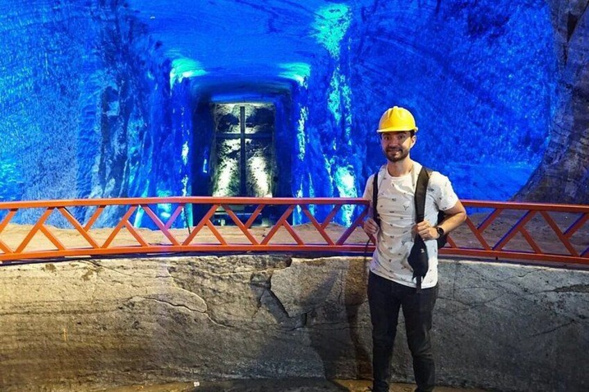 A person standing in a cave with a blue-lit tunnel and a red railing. 4