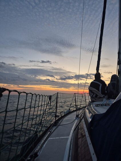 A sunset view from a boat with a netted railing and a person in a hat. 4