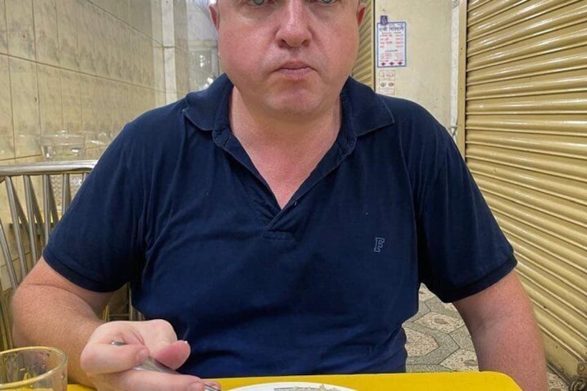 A person seated at a table with a yellow tablecloth, a glass of water, and a plate of food. 4