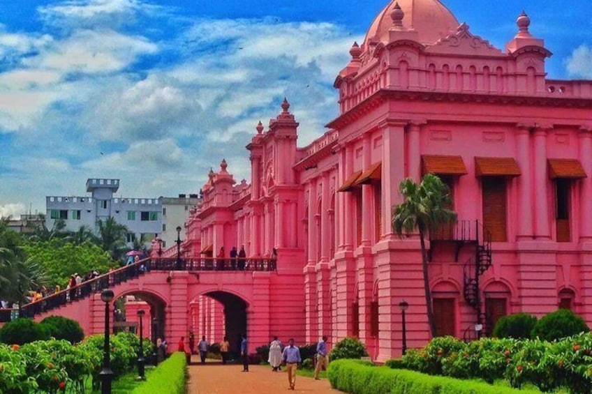 A pink colonial-style building with a dome and arches, surrounded by greenery and a clear sky. 1