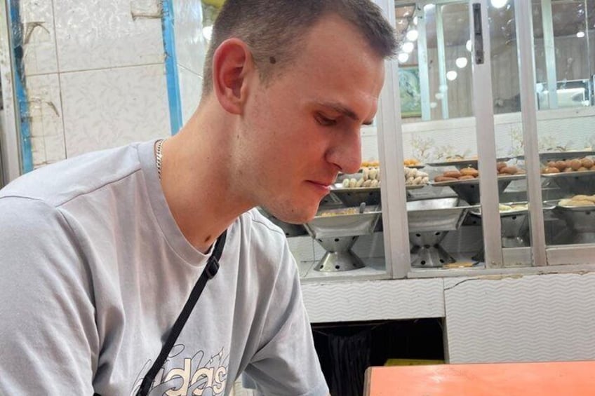 A person in a casual t-shirt with a visible logo, sitting at a table with a metal counter in the background. 3