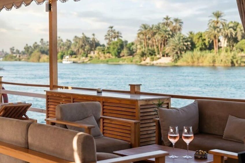 A riverside deck with wooden furniture and two glasses of wine. 2
