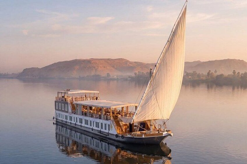 A riverboat with a large sail, calm water, and distant hills. 5