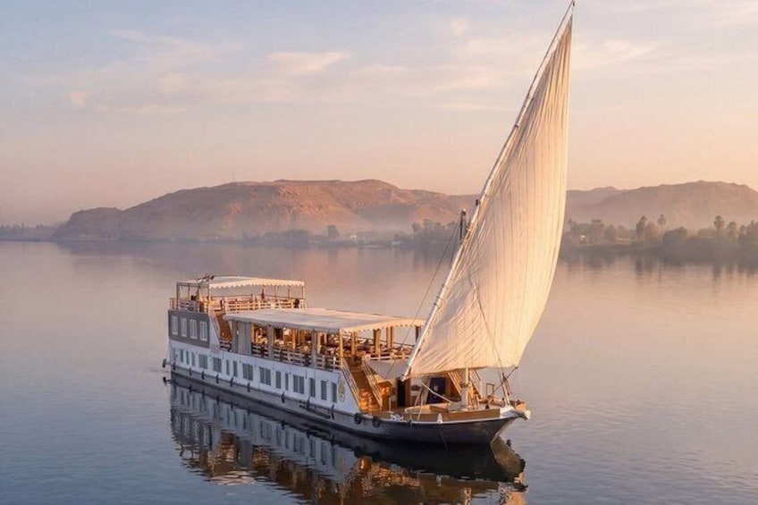 A riverboat with a large sail, docked near a calm river with hills in the background. 4