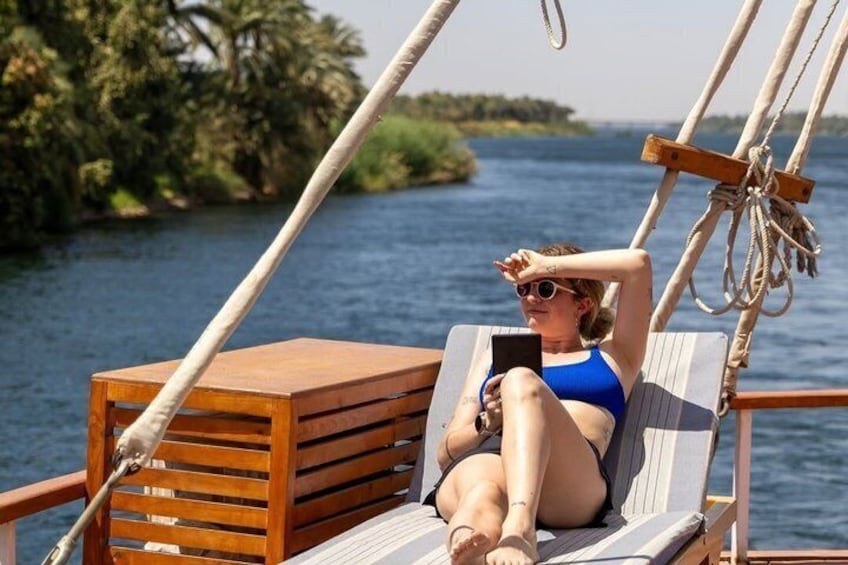 A person relaxing on a wooden deck chair on a boat, with a smartphone in hand. 5
