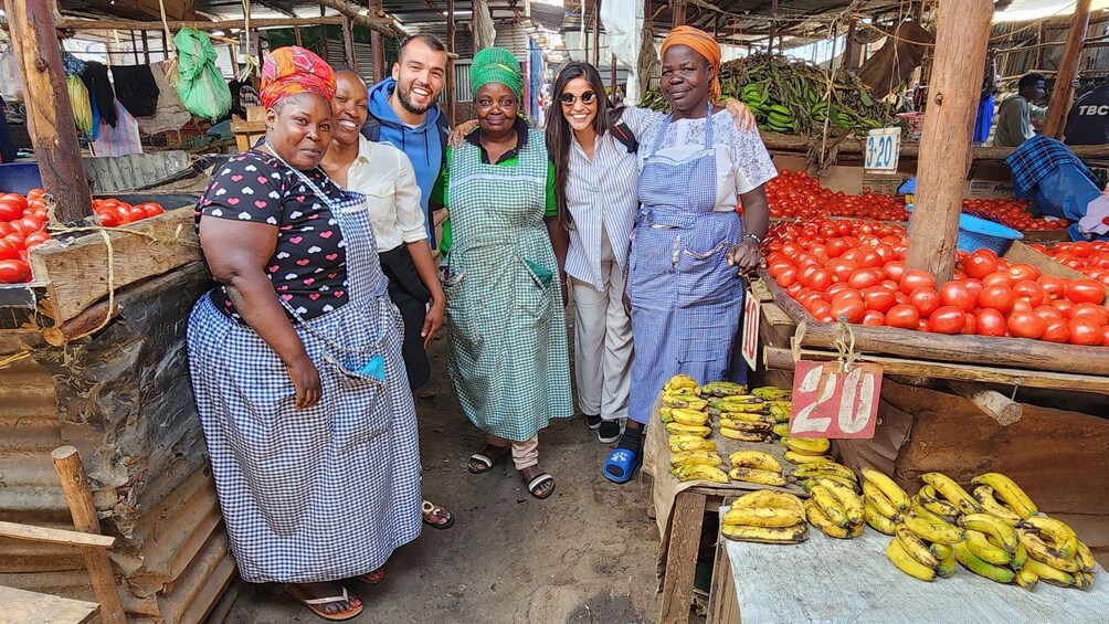 A group of people at a market with tomatoes and bananas for sale. 2