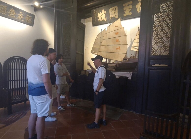 A group of people standing in front of a wall with a ship illustration and Chinese characters. 5