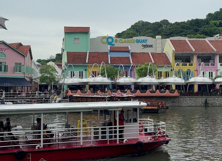 A colorful waterfront with a red boat docked, a sign for Clarke Quay, and a variety of buildings with unique architecture. 4