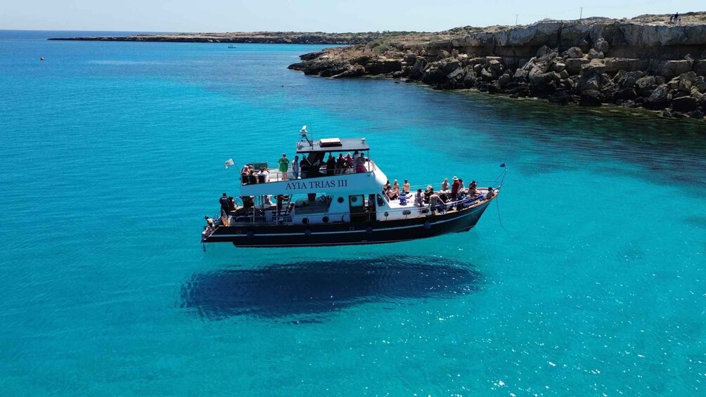A boat named 'AYIA TRIAS III' on clear turquoise waters near rocky coast. 1