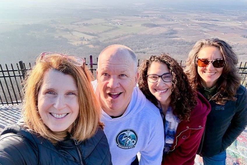 A group of people standing on a viewing platform with a scenic landscape in the background. 1
