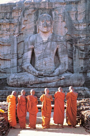 A large seated Buddha statue with monks in orange robes in front. 3
