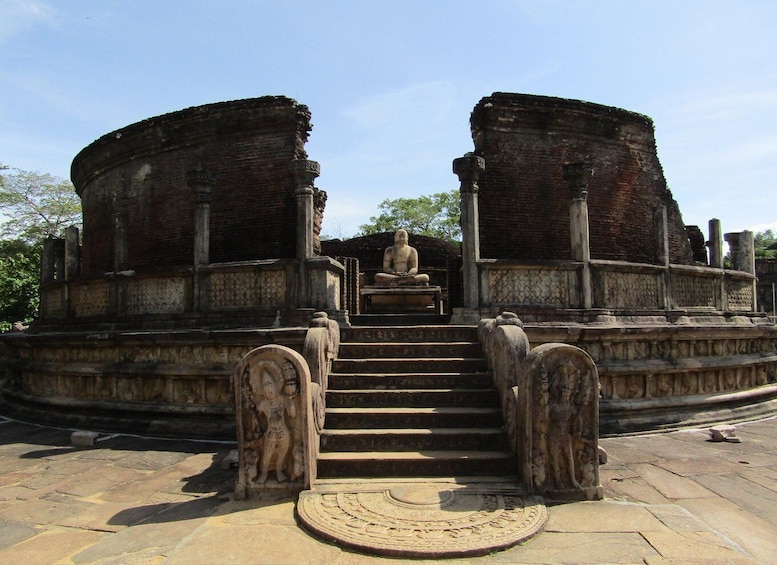 An ancient stone structure with a central seated figure, flanked by two large brick walls and a staircase leading to the figure. 2