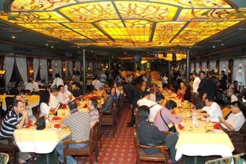 A crowded restaurant with diners seated at tables, a decorative ceiling, and a red carpet. 2
