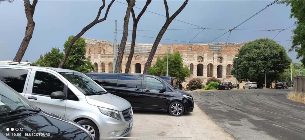A street with parked cars, a building with arches, and trees. 4