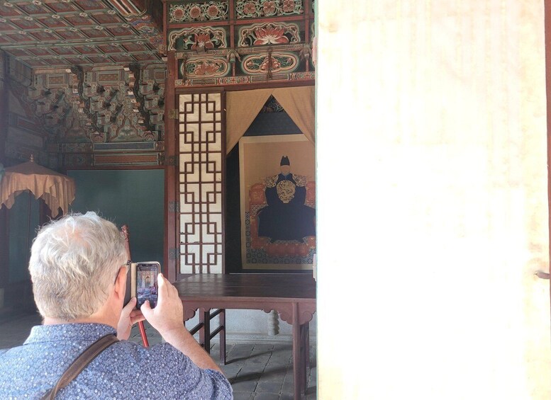 A man taking a photo of a traditional Chinese painting inside a room with ornate wooden decorations. 3