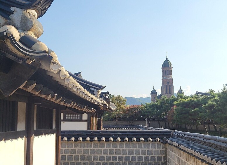 A traditional Korean building with a tiled roof and a stone wall. In the background, there is a church with a bell tower. 2