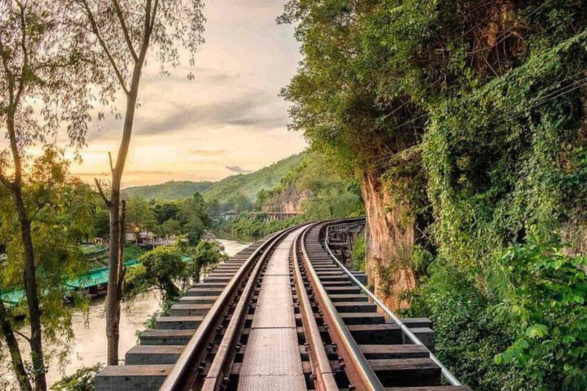 A railway track curving through a lush green landscape with a river on one side and a bridge in the distance. 4