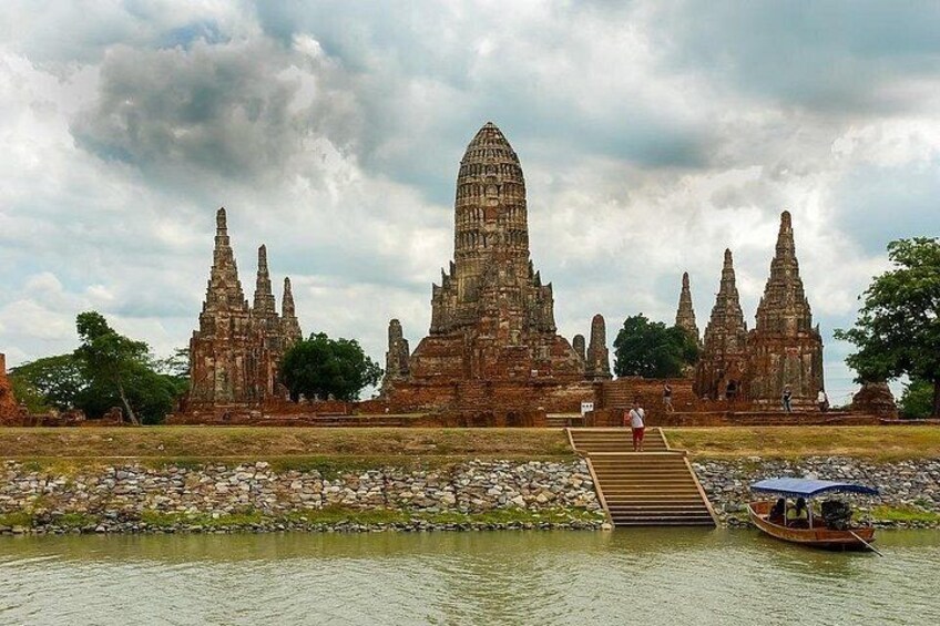 A temple complex with a central tower and smaller structures, a boat on the water, and a person walking on a bridge. 2
