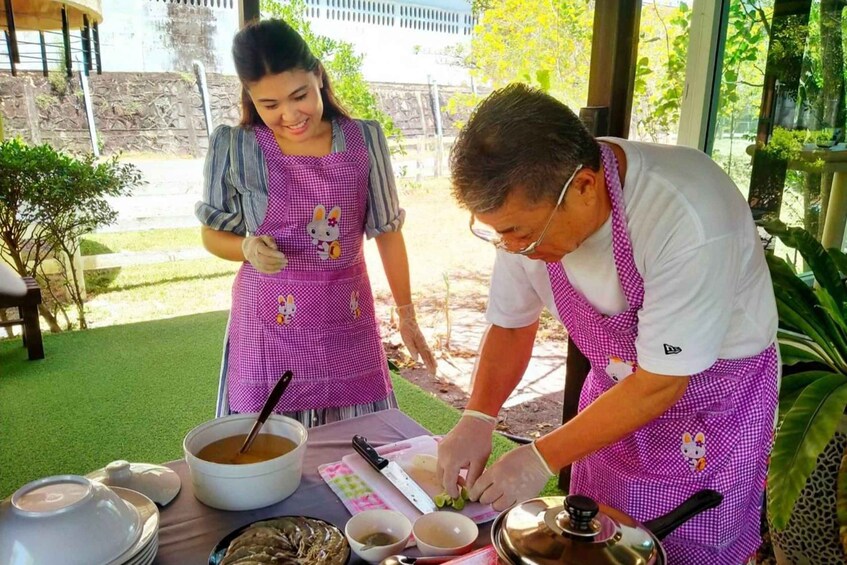 Two people in aprons preparing food outdoors with a table full of cooking utensils and ingredients. 1