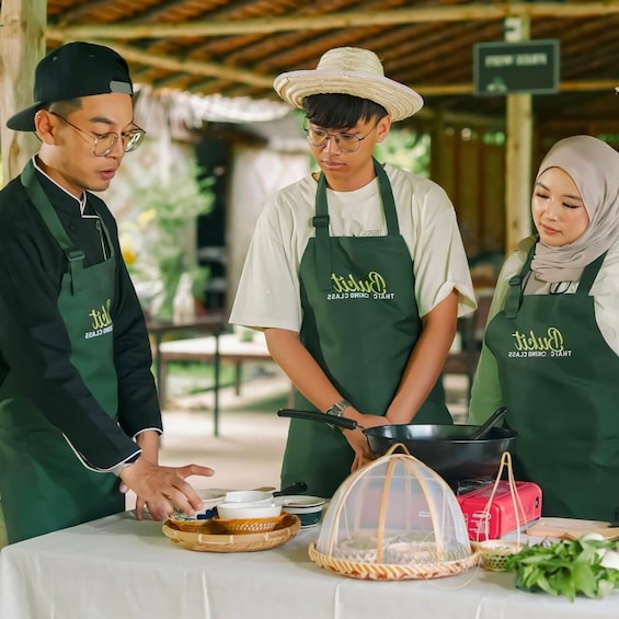 Three people wearing aprons with 'Dundie' branding, preparing food at an outdoor table with various dishes and cooking utensils. 5