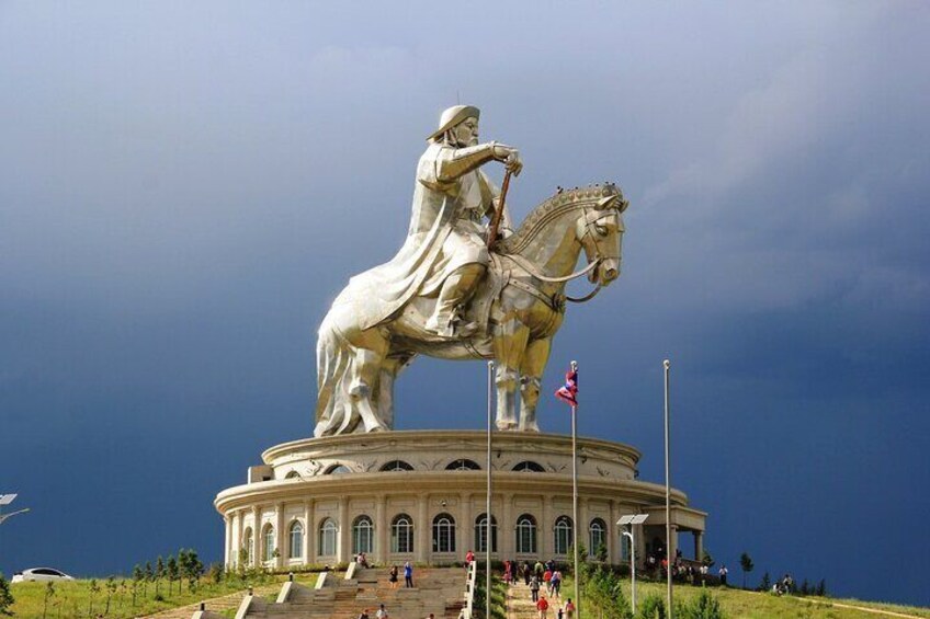 A large equestrian statue on a circular pedestal with a flag, surrounded by steps and a crowd. 4